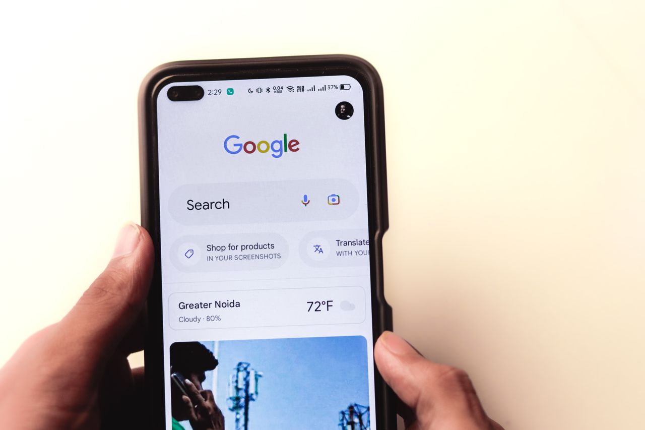 services-01 A close-up of a hand holding a smartphone with Google search displayed on the screen.